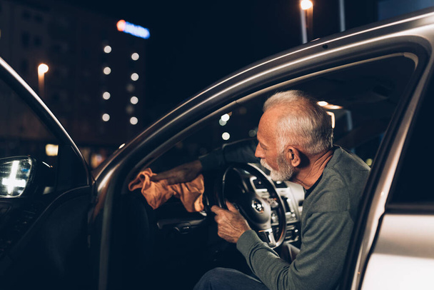 Dettaglio interno auto. Senior barba uomo pulizia la sua auto la sera alla stazione di autolavaggio. - Foto, immagini