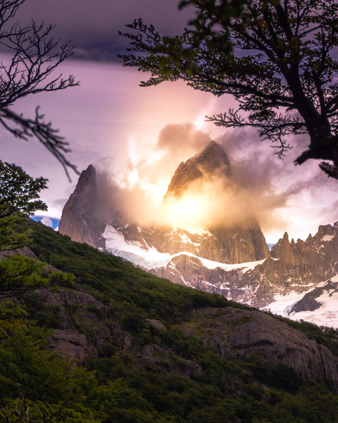 Svislé skalnaté zasněžené vrcholky hor, za nimiž se zvedá slunce a rudé mraky. Fitz Roy v Argentině - Fotografie, Obrázek