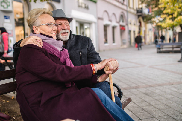 Mature husband and wife enjoying together while sitting on bench in the city. - Photo, Image