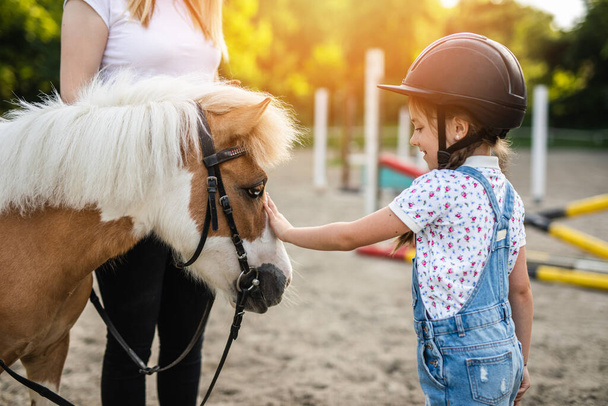 Симпатична маленька дівчинка і її старша сестра насолоджуються поні конем на свіжому повітрі на ранчо
 - Фото, зображення