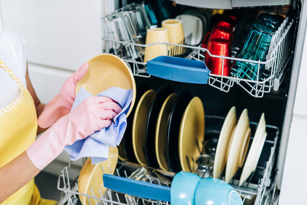 Közelkép női kézről, amint mosogatógépből vesz ki tiszta edényeket.. - Fotó, kép