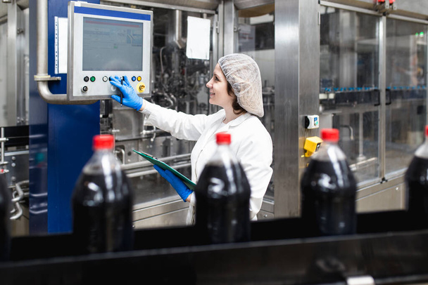 Молода щаслива жінка-працівник на фабриці з перевірки пляшок соку перед відправкою. Контроль якості інспекції
.  - Фото, зображення