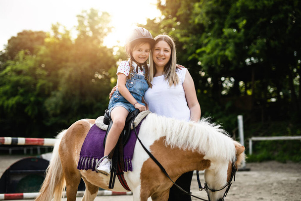 Cute little girl and her older sister enjoying with pony horse outdoors at ranch. - 写真・画像