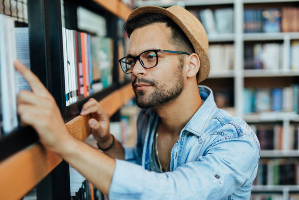 Aantrekkelijke jonge mannelijke student die boeken kiest in de boekhandel - Foto, afbeelding