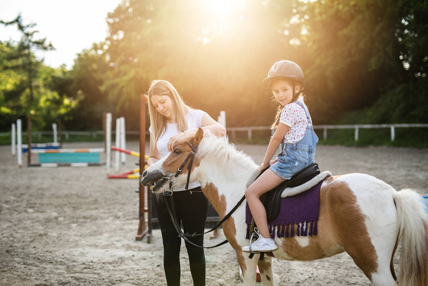Cute little girl and her older sister enjoying with pony horse outdoors at ranch. - Fotoğraf, Görsel