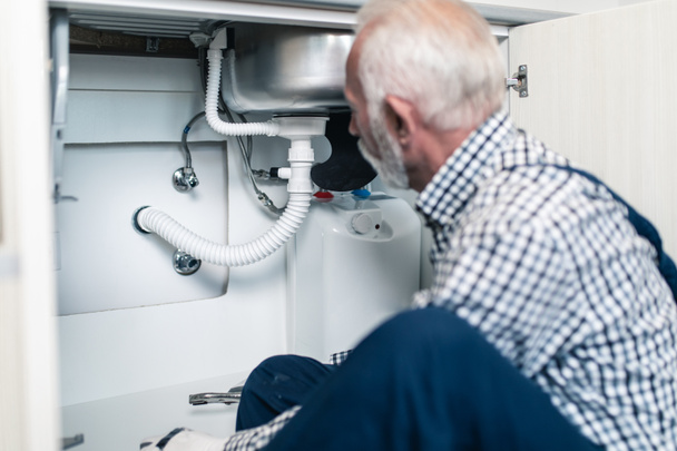 Senior loodgieter werkt met sanitair gereedschap in de keuken. Renovatie. - Foto, afbeelding