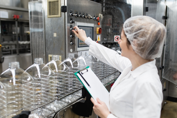 Vrouwelijke werknemer in bottelarij die waterflessen controleert voor verzending. Inspectiekwaliteitscontrole.  - Foto, afbeelding