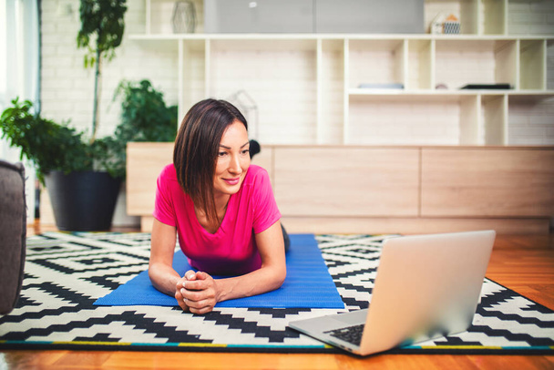 Женщина смотрит онлайн-уроки на ноутбуке, занимаясь дома в гостиной. - Фото, изображение