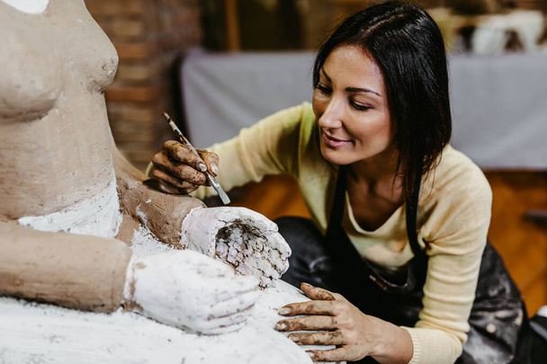 Mooie middelbare leeftijd vrouw professionele beeldhouwer werken aan prachtige beeldhouwkunst. - Foto, afbeelding