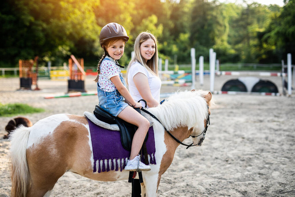 Χαριτωμένο κοριτσάκι και η μεγαλύτερη αδελφή της απολαμβάνουν με πόνυ άλογο σε εξωτερικούς χώρους στο ράντσο. - Φωτογραφία, εικόνα