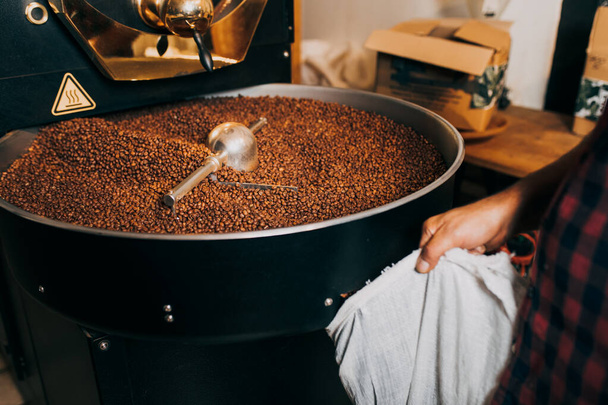 Man's hands holding freshly roasted aromatic coffee beans over a modern coffee roasting machine. - Photo, image