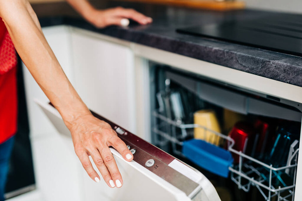 Close up shot of woman's hand taking out clean dishes from dishwasher machine. - Foto, Imagen