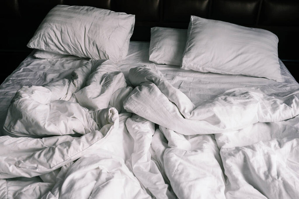 白いリネンで手付かずの空のベッド。1泊分の睡眠後にアパートやホテルのシーツや枕。ホテルの汚くて崩れかけた毛布. - 写真・画像