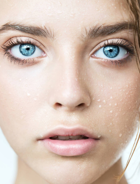Close up of young woman face  with clean perfect skin and water moisture drops. Macro portrait of beauty model with natural nude makeup moisturizing her skin by lotion. Spa, skincare and wellness. Close up, background, copy space. - Foto, Imagem