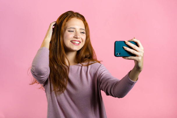 Smiling happy woman making selfie on smartphone over pink background. Technology, mobile device, social networks concept - Foto, Imagem
