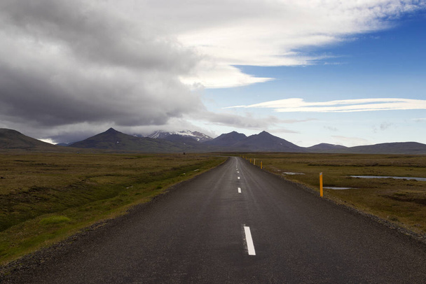 Dramatická islandská krajina. Pohled na temnou asfaltovou silnici s divokým prázdným polem a horským zázemím. Východní Island. - Fotografie, Obrázek