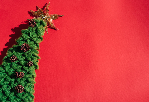 Beautiful red gradient Christmas background and lots of empty space for text. Handmade green knitted Christmas tree with a gold tinsel star on top and small pine cones. - Photo, Image