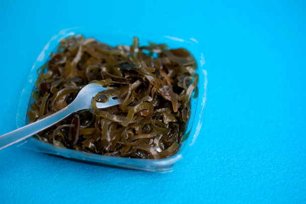 Вкусный салат из свежих водорослей. Съедобный салат из морских водорослей и вилка на синем фоне. - Фото, изображение