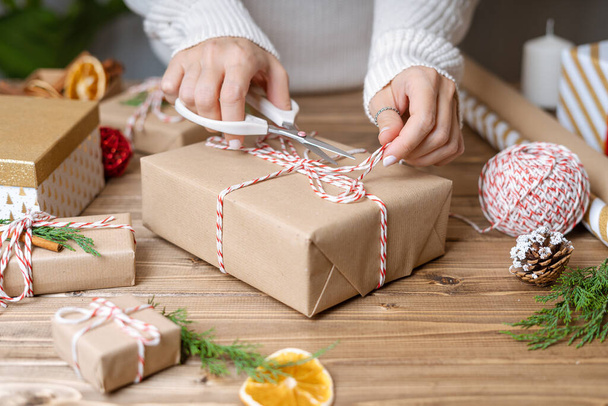 Női kezek csomagolása karácsonyi ajándék, közelről. Felkészületlen ajándékok fa háttér díszítő elemek és elemek, felülnézet. Karácsony vagy újév DIY csomagolási koncepció. Lépésről lépésre - Fotó, kép