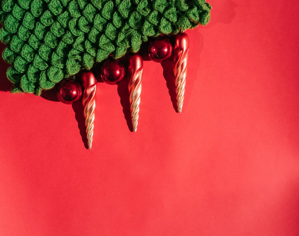 Όμορφη κόκκινη κλίση Χριστουγεννιάτικο φόντο και πολύ κενό χώρο για κείμενο. Πράσινο χειροποίητο πλεκτό χριστουγεννιάτικο δέντρο με χριστουγεννιάτικα παιχνίδια σε σχήμα πορτοκαλί icicles και κόκκινες γυαλιστερές μπάλες. - Φωτογραφία, εικόνα