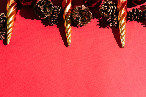 Schöner roter Hintergrund und viel Platz für Text. Weihnachtsbaumspielzeug in Form orangefarbener Eiszapfen, rot glänzende Kugeln und dekorative Tannenzapfen sind obenauf. - Foto, Bild