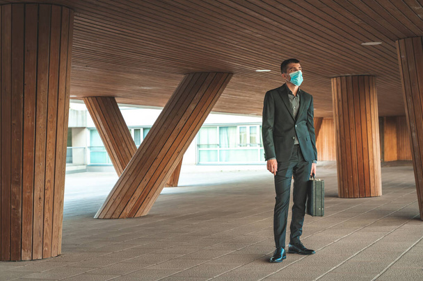 Confident and successful. Handsome young businessman wearing surgical face mask, looking away standing outdoors with office building in the background - Φωτογραφία, εικόνα