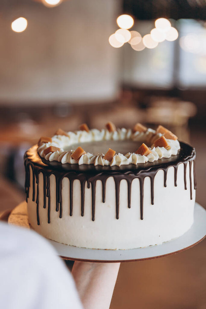 appetizing big white cake with chocolate and caramel on a cafe background - Foto, Imagem