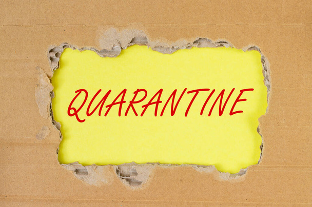 word QUARANTINE on yellow table through torn craft paper, flatly, top view. - Foto, Imagem