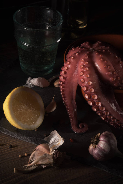 Mediterranean seafood. Whole fresh raw octopus with lemon and garlick, rustic background, side view. - Photo, image