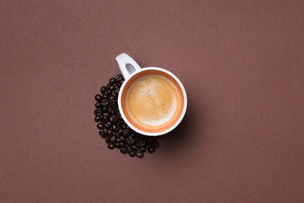 A top view of a fresh espresso cup surrounded by coffee beans on brown background - 写真・画像