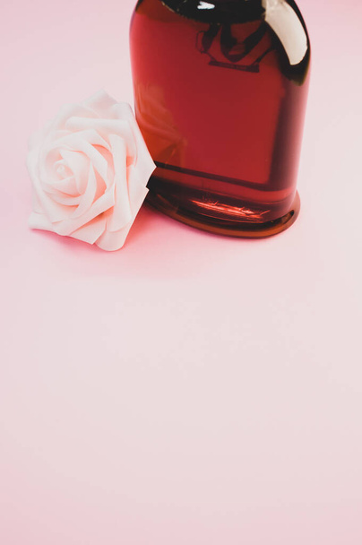 A bottle of nice perfume with a beautiful rose flower on a pink background - Фото, изображение