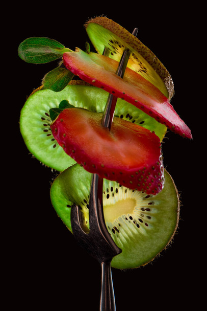 Sliced fresh and juicy green kiwi and red strawberry on the silver fork on dark background. healthy food concept. close up. low key. - Foto, Imagem