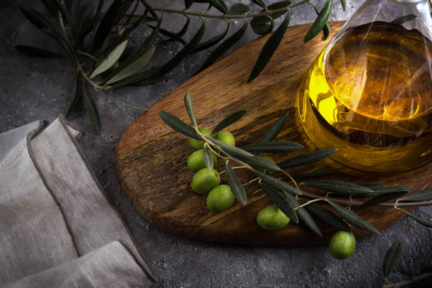 Extra virgin olive oil in glass bottle with branch of olives on rustic background. low key. close up view - 写真・画像