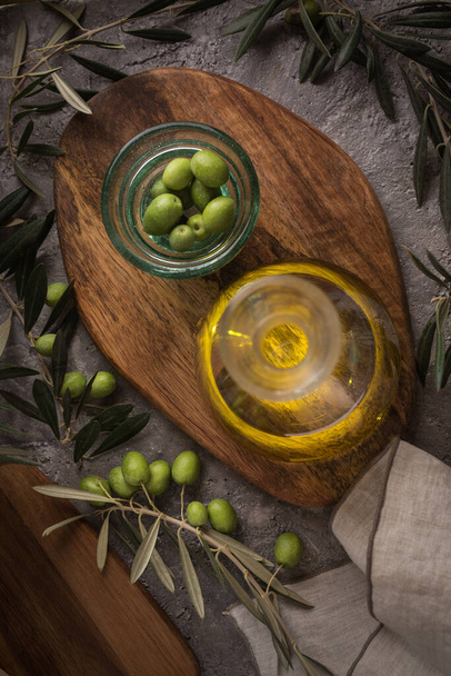 Extra vierge olijfolie in glazen fles met olijftak op rustieke achtergrond. Rustig aan. vlakke lay - Foto, afbeelding