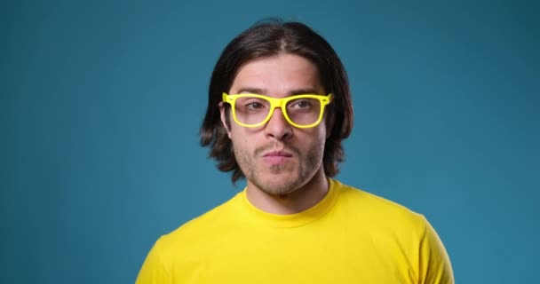Mężczyzna w żółtych okularach tańczy na niebieskim tle - Materiał filmowy, wideo