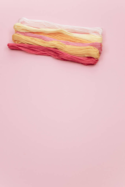 A vertical shot of colorful mouline threads isolated on a light pink background - Foto, afbeelding