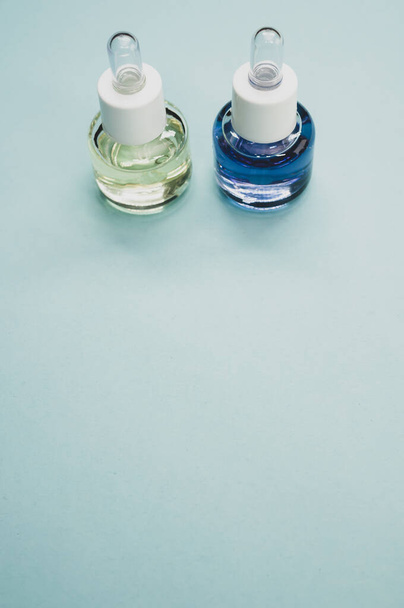 A vertical shot of two bottles of essential oil placed on a blue surface - Фото, изображение