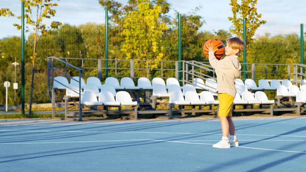 Kleine jongen basketbal spelen op het veld buiten - Foto, afbeelding
