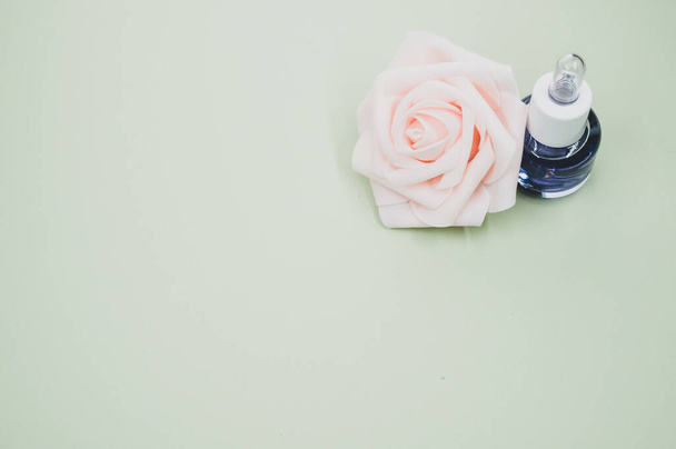 A high angle shot of a bottle of essential oil next to a beautiful pink rose placed on a gray surface - Foto, Imagen