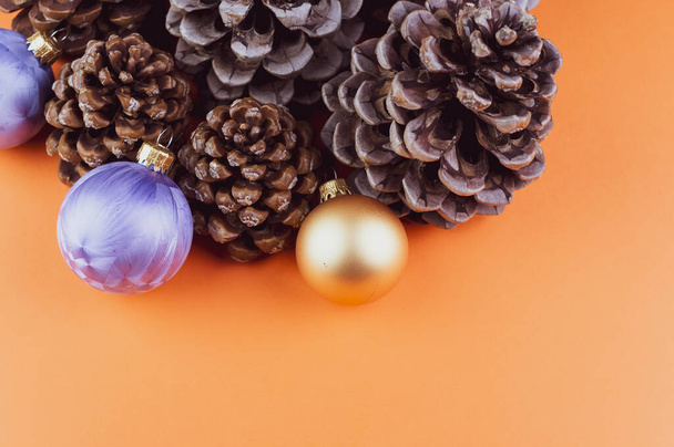A high angle shot of assorted decorative pine cones, gold and purple Christmas ornaments on an orange surface - Photo, Image