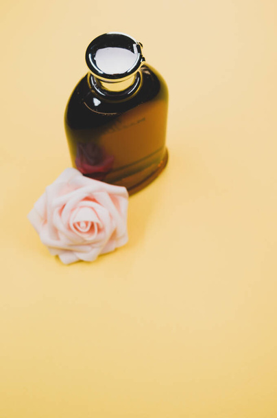 A bottle of nice perfume with a beautiful rose flower on a yellow background - Photo, image