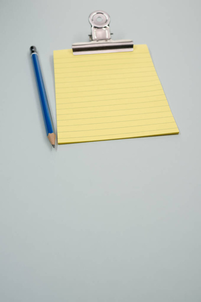 Una toma vertical de un bloc de notas con un cortapapeles y un lápiz aislados sobre un fondo gris - Foto, imagen