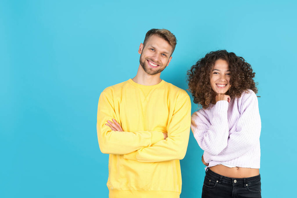 Happy mixed race man and woman looking at camera, smiling wide. Two confident friends standing together isolated on blue copy space background - Photo, Image