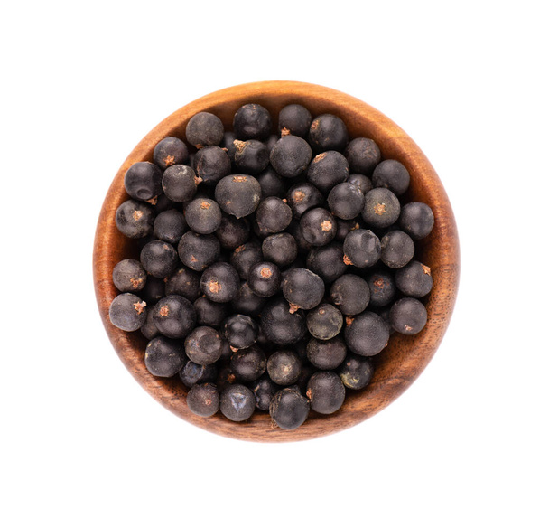 Dry juniper berries in wooden bowl, isolated on white background. Top view - Photo, Image