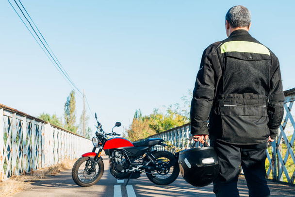 mies selällään katsomassa moottoripyörää kypärä kädessään - Valokuva, kuva