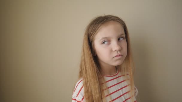 Little tired girl with long blonde hair posing to camera and swinging her body from side to side at room. Portrait of small bored child against the background of beige wall. Close up Slow motion - Footage, Video