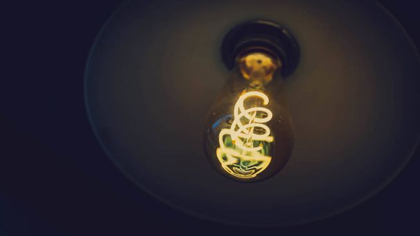 A low angle shot of an old-style vintage glowing light bulb in a dark setting - Zdjęcie, obraz