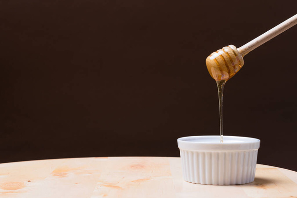 A wooden honey dipper flowing into a bowl on dark background - 写真・画像