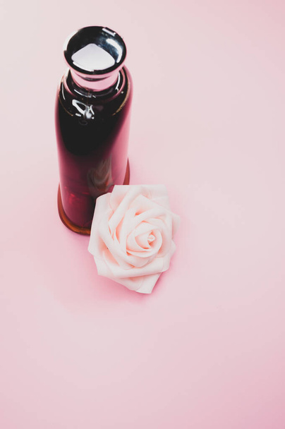 A bottle of nice perfume with a beautiful rose flower on a pink background - Foto, imagen