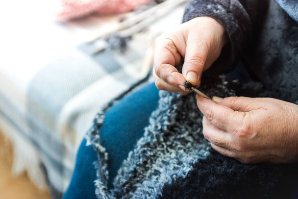 A closeup shot of a woman sitting on the couch at home and knitting a gray and black scarf - Fotoğraf, Görsel